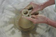 Hands molding clay on a pottery wheel under soft natural light.