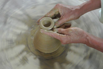 Hands shaping clay on a pottery wheel surrounded by focused team members sharing smiles.