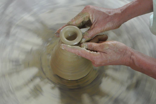 A diverse group of Indian professionals shaping clay together around a pottery wheel in a warm, elegant studio.