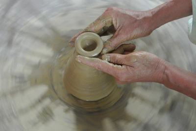 Hands shaping a clay heart on a potter’s wheel in soft natural light.