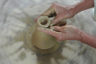 Hands molding clay on a pottery wheel, with the clay spinning under skilled fingers and the surrounding area blurred from motion.