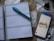 A spiral-bound planner is opened to a blank page with lines for daily entries. A blue pen is placed on top of the planner. Next to it, there is a smartphone with a colorful chart displayed on the screen. In the background, a smartwatch with a white strap is visible on a patterned surface.