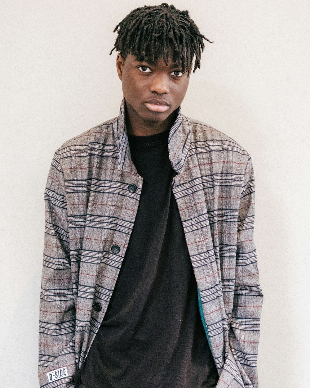 a man with dreadlocks standing in front of a white wall