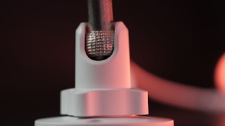 A close-up of a metallic component featuring a textured grid pattern, partially encased in a smooth white holder. The lighting casts a warm glow on the surface, highlighting details and creating a soft gradient in the background.