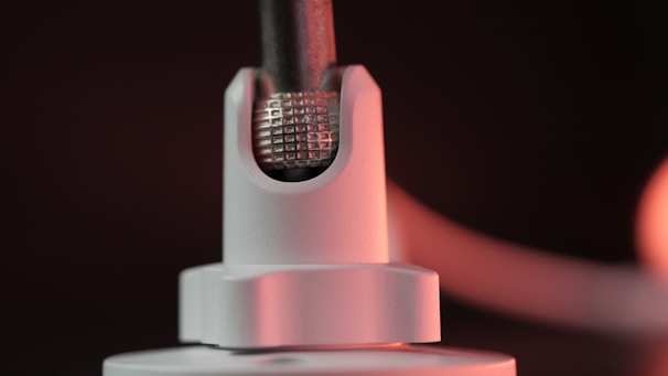 A close-up of a metallic component featuring a textured grid pattern, partially encased in a smooth white holder. The lighting casts a warm glow on the surface, highlighting details and creating a soft gradient in the background.