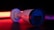 A surveillance camera is in focus, bathed in dramatic lighting with strong red and black tones. The brand name on the side is visible, and the camera's lens is slightly reflective. The background is dark, enhancing the illuminated effect of the camera.