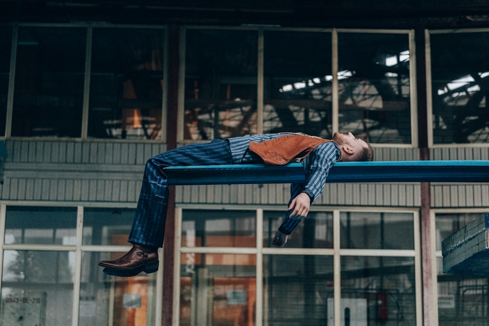 a man laying on a blue bench in front of a building