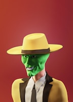 A cartoonish character with a bright green face wearing a large yellow hat and a matching yellow suit with a black trim. The background is a gradient of warm red tones, and the character displays a mischievous smile.