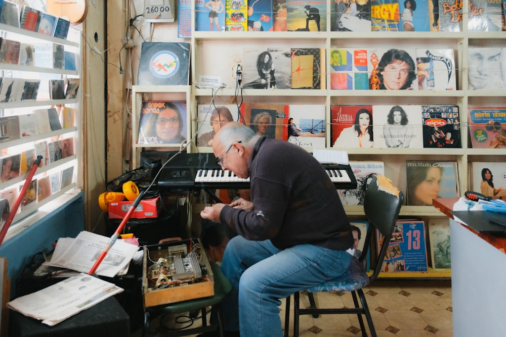 a man sitting at a piano in front of a wall of records