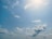A clear blue sky with scattered, fluffy white clouds. The sun is shining brightly, casting a soft glow, and there are no visible objects or people.