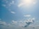 A clear blue sky with scattered, fluffy white clouds. The sun is shining brightly, casting a soft glow, and there are no visible objects or people.
