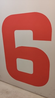 Large red number six painted on a plain wall, slightly worn or dirty at the bottom corner.