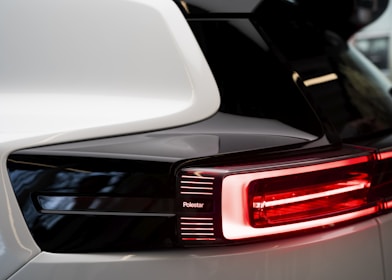 Close-up view of a car's rear light with sleek and modern design elements, featuring a prominent black and white color scheme. The brand name 'Polestar' appears next to the glowing red lights, indicating a focus on a contemporary and high-tech aesthetic.