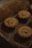A group of three small pies with intricate patterns on their tops rests on crumpled parchment paper within a container. The scene is dimly lit, suggesting a warm and cozy setting.