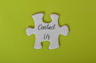 A white jigsaw puzzle piece with the words 'Contact Us' written on it is set against a bright lime green background.