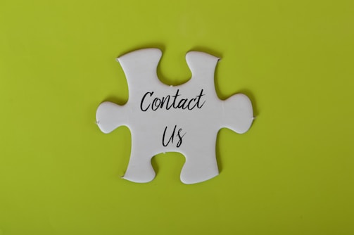 A white jigsaw puzzle piece with the words 'Contact Us' written on it is set against a bright lime green background.