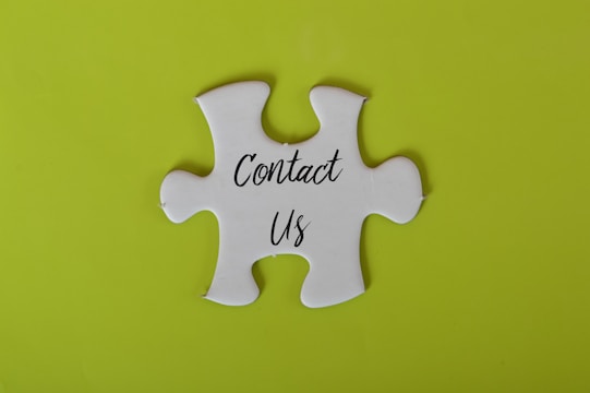 A white jigsaw puzzle piece with the words 'Contact Us' written on it is set against a bright lime green background.
