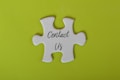 A white jigsaw puzzle piece with the words 'Contact Us' written on it is set against a bright lime green background.