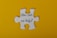 A large white puzzle piece is centered against a bright yellow background. The text 'How can we help?' is written in black, elegant script on the puzzle piece.
