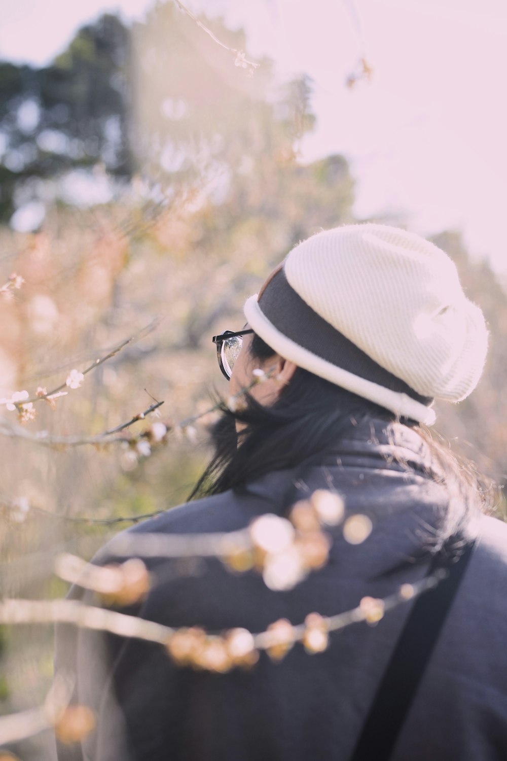 a woman wearing a hat and glasses standing next to a tree