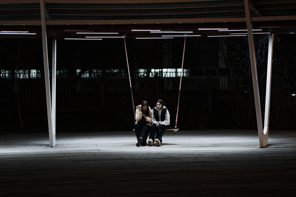 two people sitting on a swing in the dark