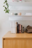 A wooden minimalist office bookshelf holding neatly arranged books and plants.