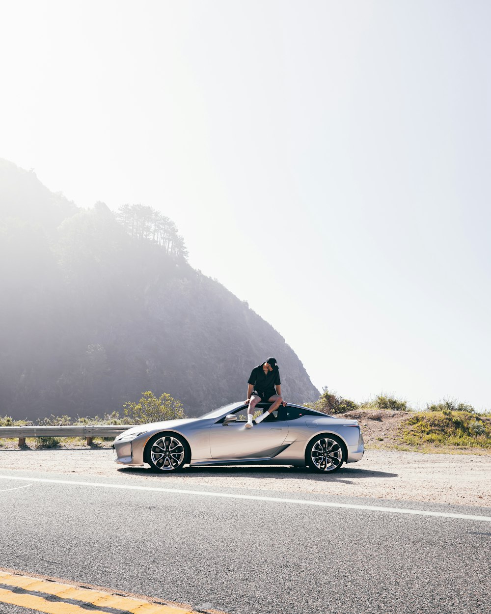 a man sitting on top of a silver sports car