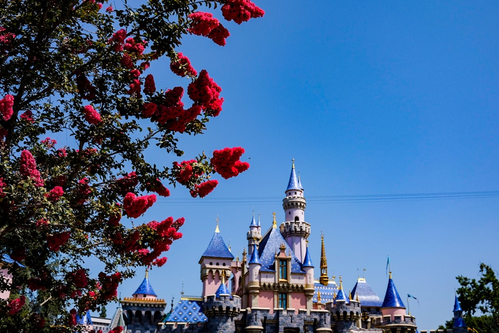 a pink castle with a blue roof surrounded by red flowers