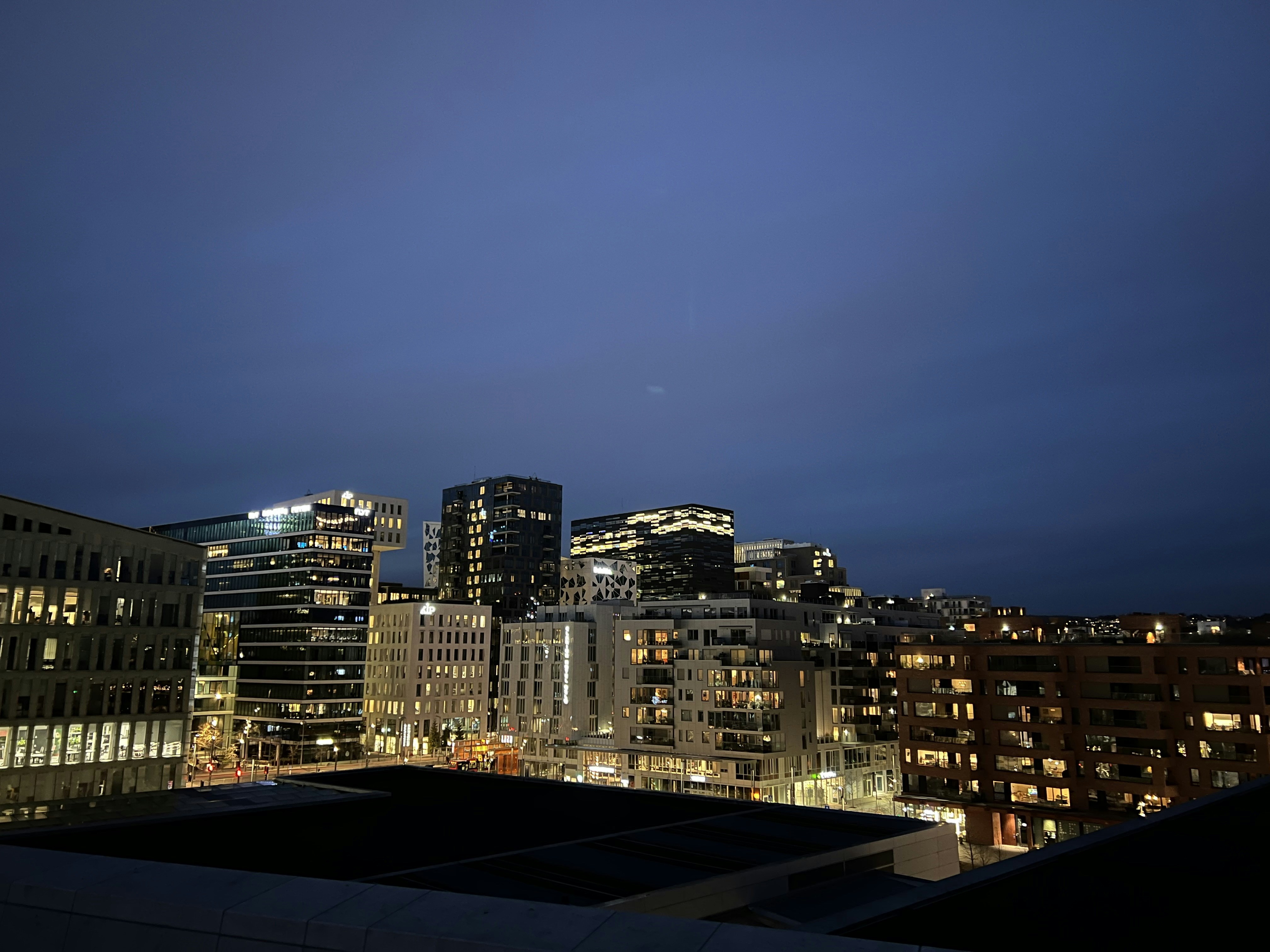 Modern city skyline with residential buildings at dusk, warm amber street lights, soft focus background