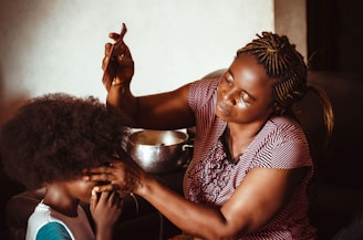 A stylist carefully braiding a client's natural hair in a cozy, inviting salon setting.