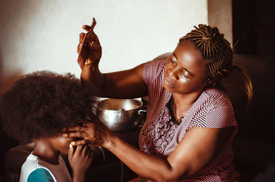 Close-up of hands expertly braiding natural curly hair with warm lighting.