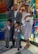 A family poses for a photo in front of a colorful stained glass background. The family consists of two adults and three children. The adults are dressed in formal attire, with the man adjusting his glasses and the woman holding a baby. The two older children are also in suits, looking attentively at the camera.