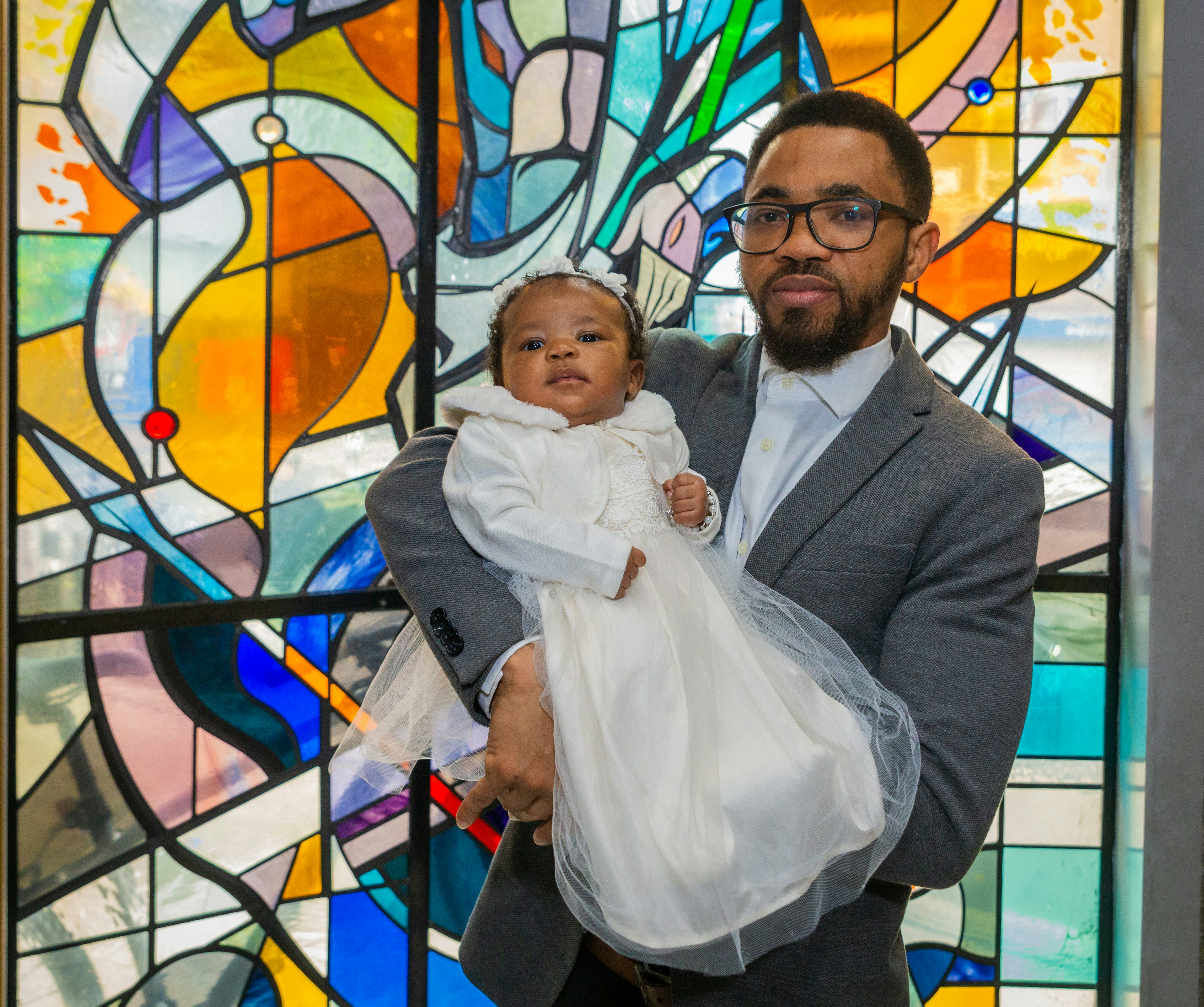a man holding a baby in front of a stained glass window