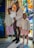 Three children and a baby are standing in front of a vibrant stained glass background. The older child is holding the baby, who is dressed in white, while the two younger children stand on either side, wearing pastel-colored outfits and smiling.