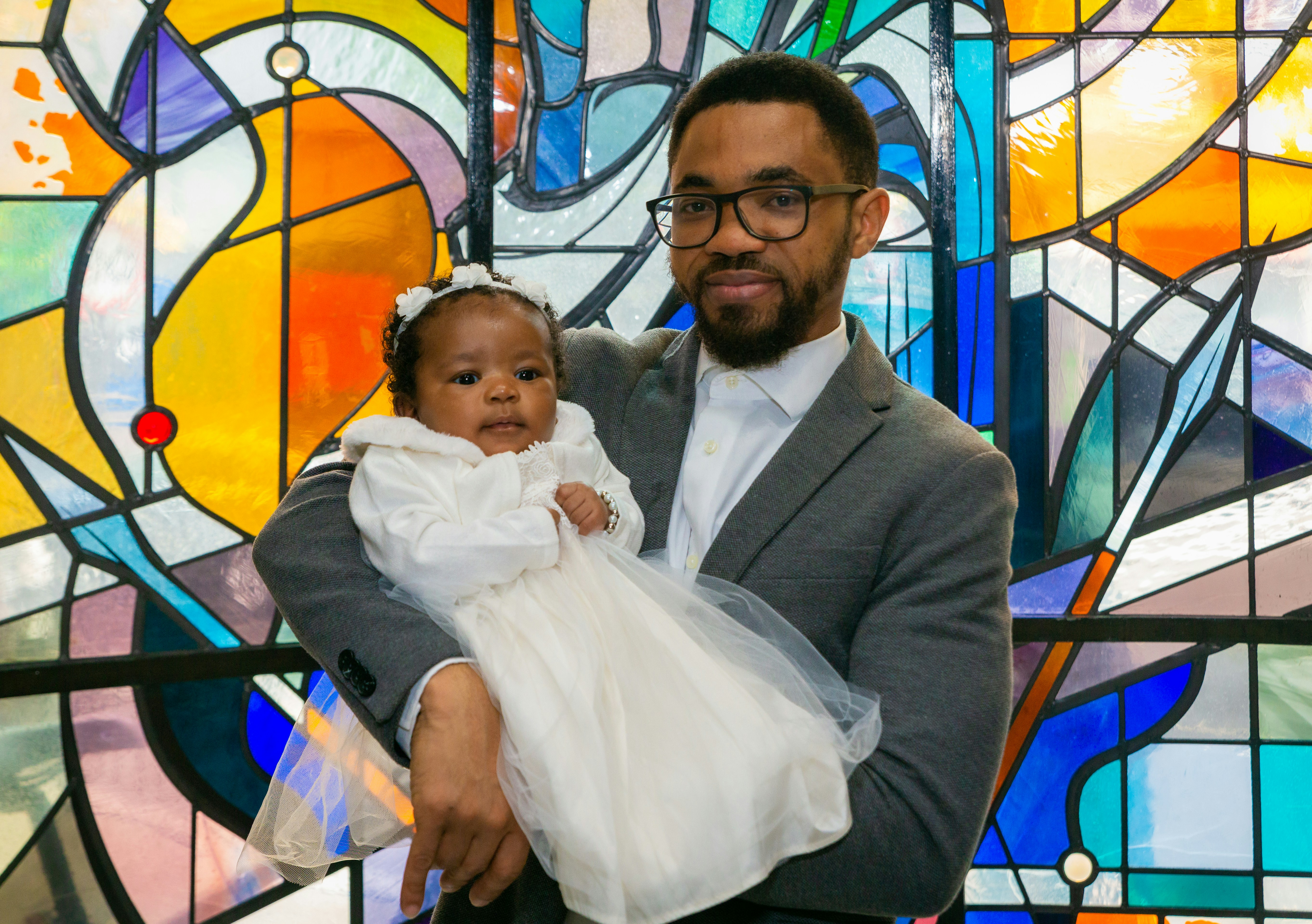 a man holding a baby in front of a stained glass window