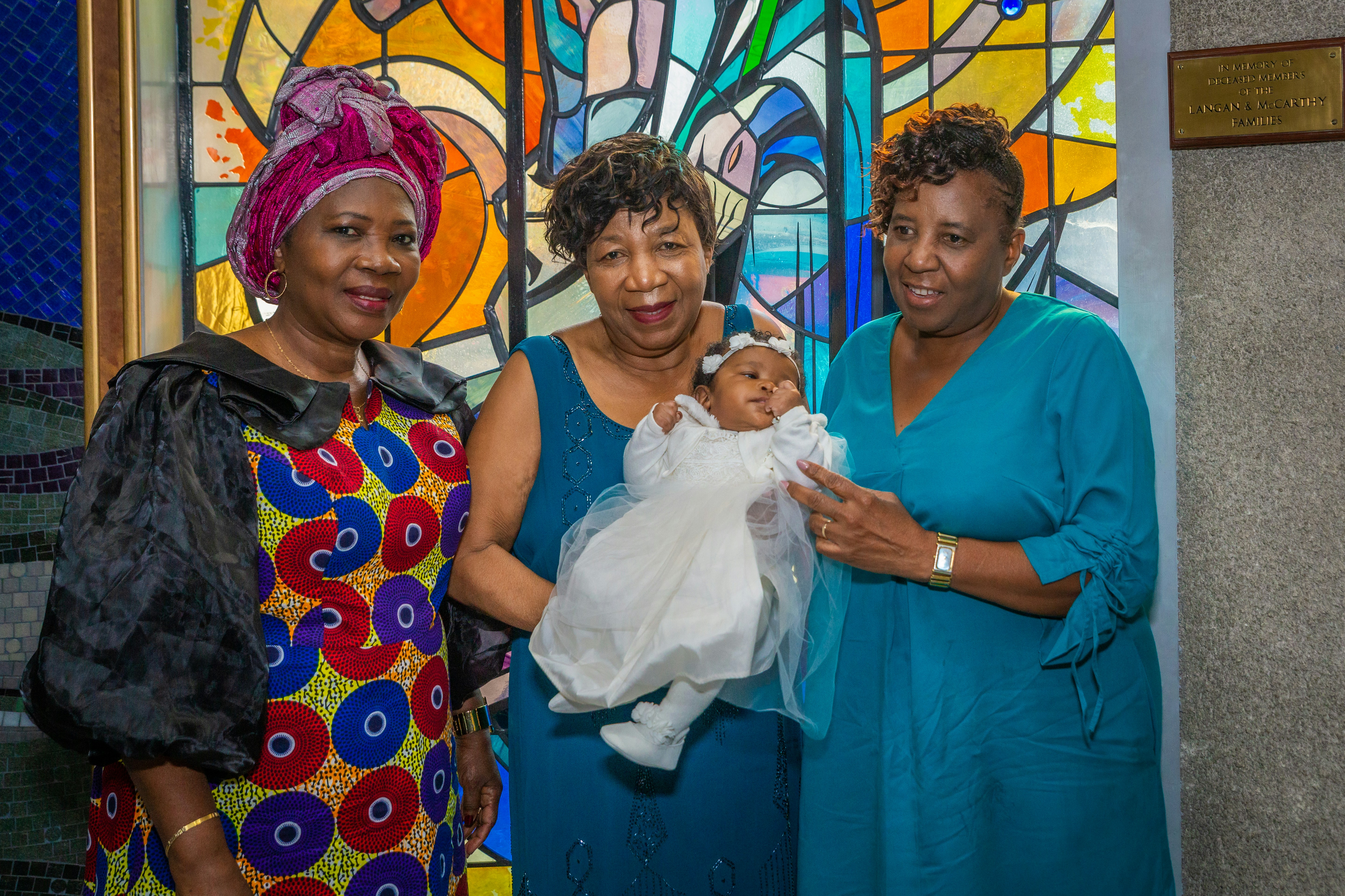 three women holding a baby in front of a stained glass window