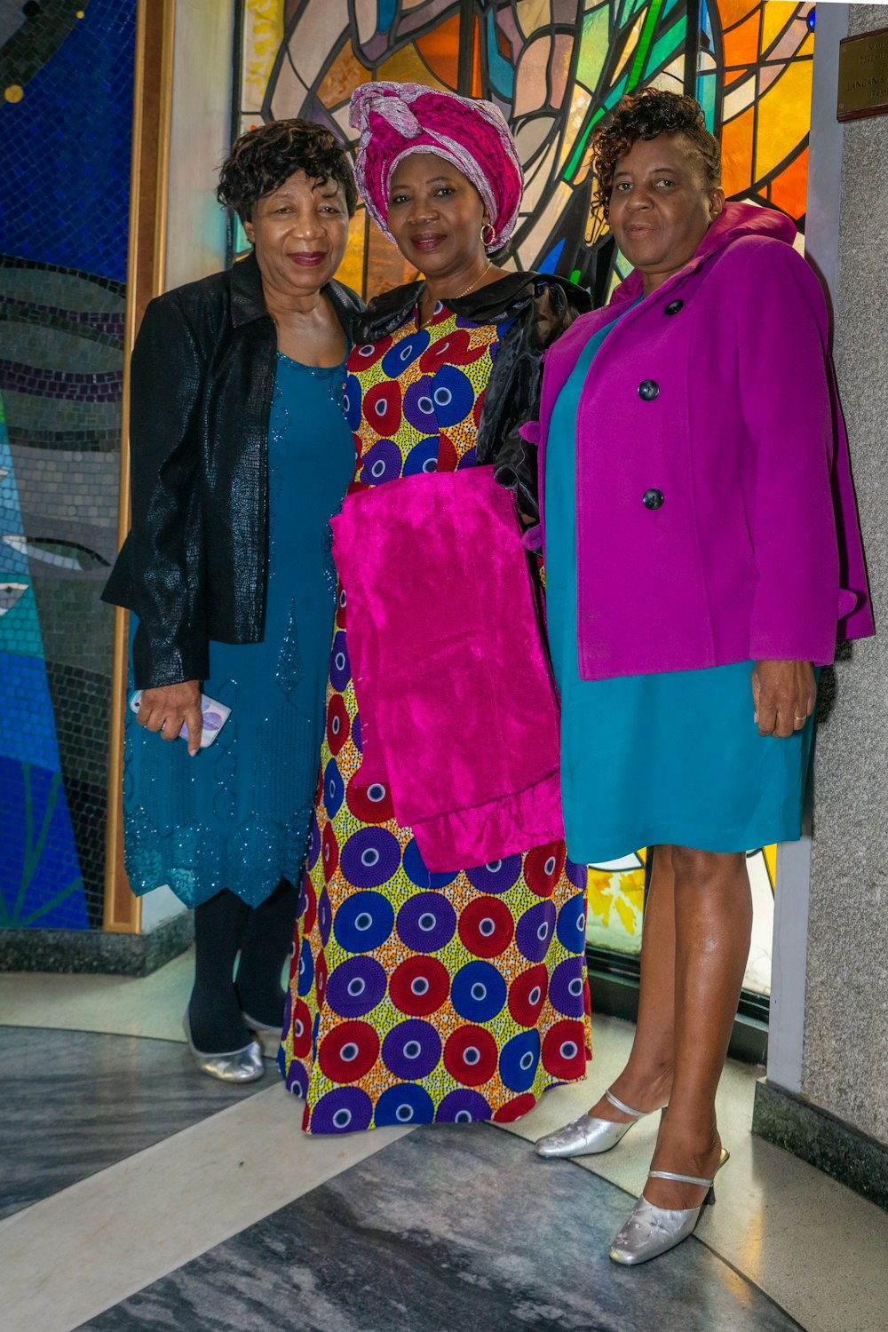 three women standing next to each other in front of a stained glass window