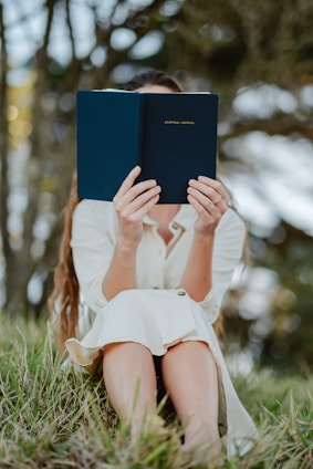 A serene woman sitting outdoors with a Bible and journal, reflecting in peaceful nature.