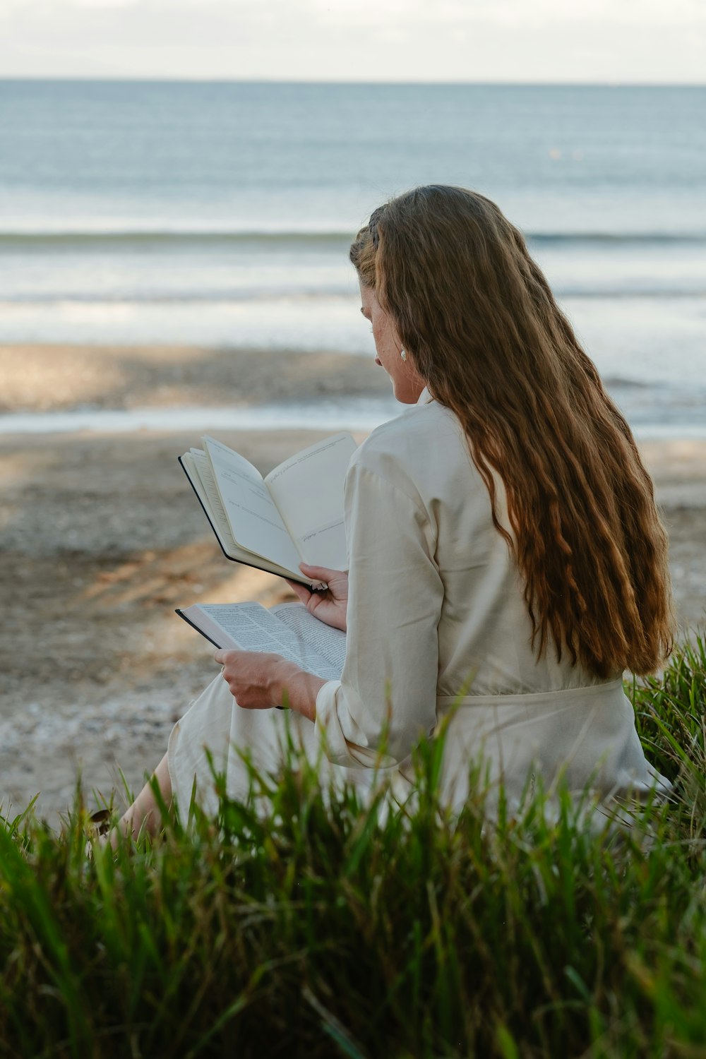 a woman sitting on the beach reading a book