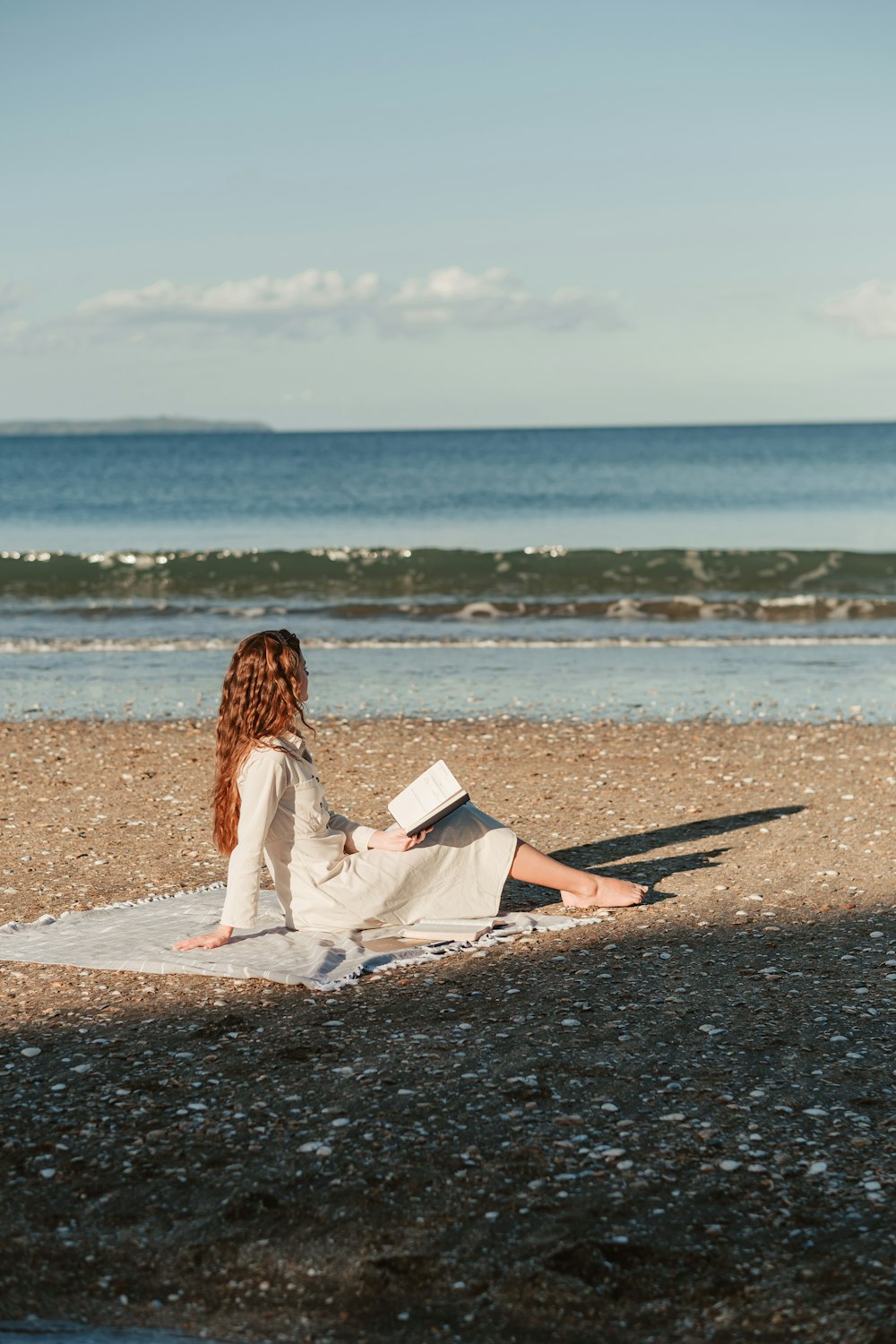 una donna seduta su una spiaggia che legge un libro