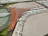 A scale model of an airport terminal featuring a large, brown, V-shaped building with numerous parked airplanes lined up along the terminal gates. The surrounding area includes a series of roads, greenery, and a circular section with multiple lanes and vehicles.