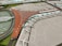 A scale model of an airport terminal featuring a large, brown, V-shaped building with numerous parked airplanes lined up along the terminal gates. The surrounding area includes a series of roads, greenery, and a circular section with multiple lanes and vehicles.