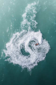 A person riding a jet ski creates a swirling pattern of white water against a backdrop of turquoise sea. The circular trail in the water draws attention, showing a dynamic contrast between the calm water and the swiftly moving vehicle.