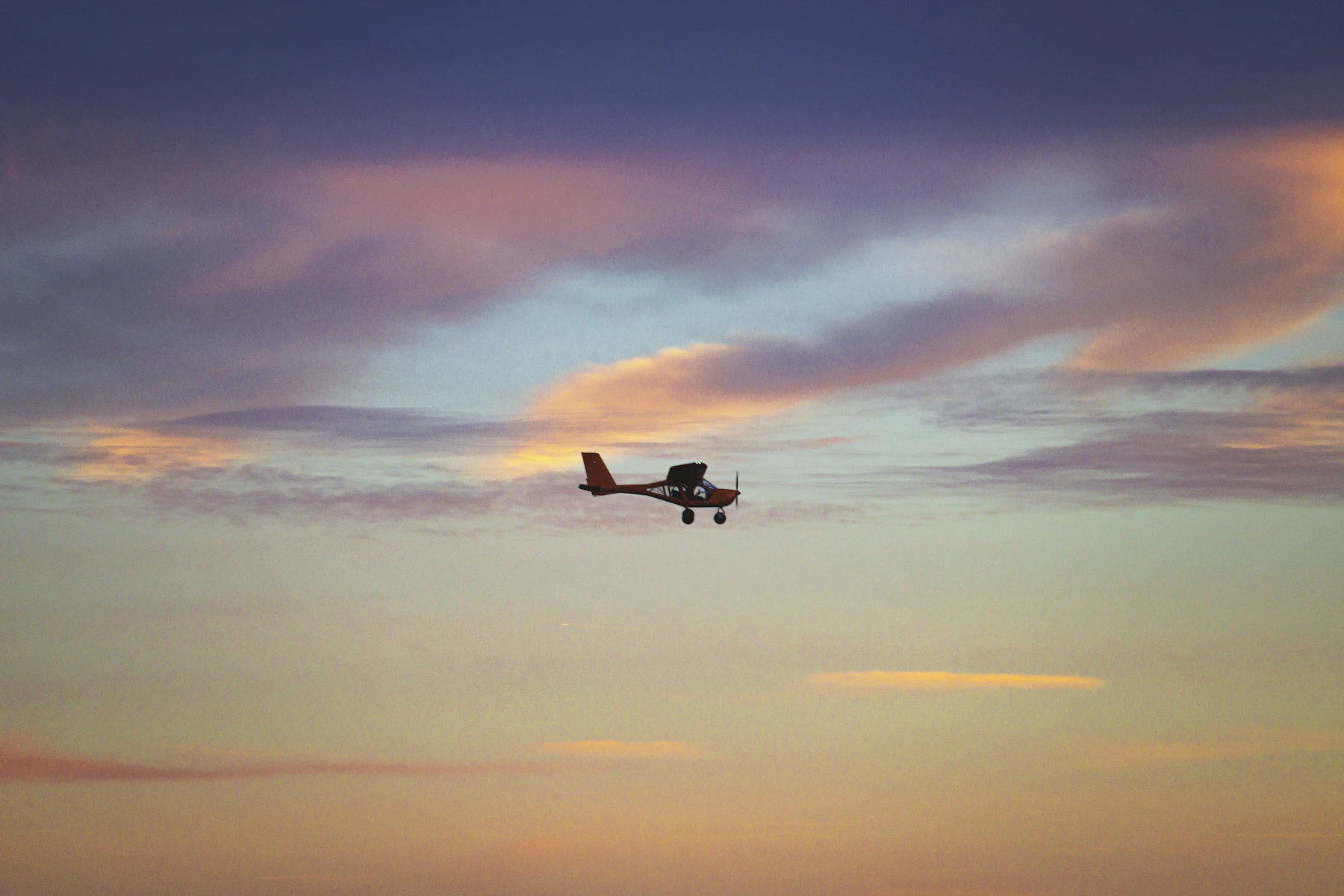 A light aircraft silhouetted against a pastel sunset