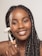 A person with braided hair is smiling while using a facial roller on their cheek. The roller has a white and gold handle, and the background is neutral.