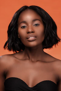 Professional portrait of Isis Delboni smiling warmly against a clean, modern background with subtle orange and black tones.