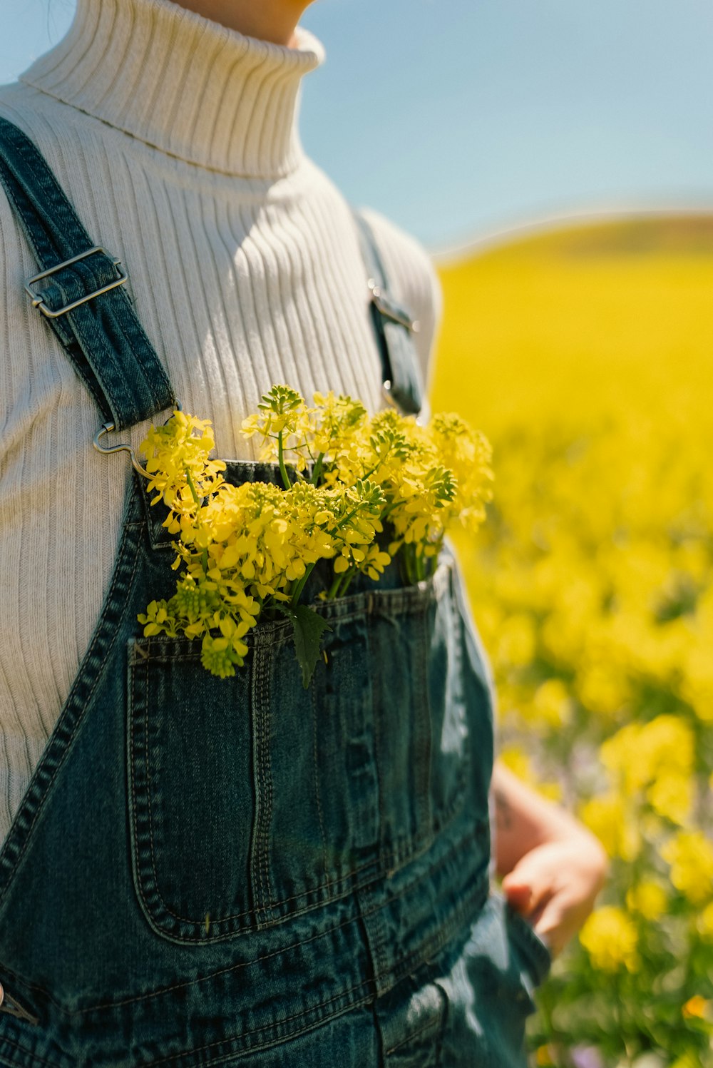 a woman in overalls holding a yellow flower