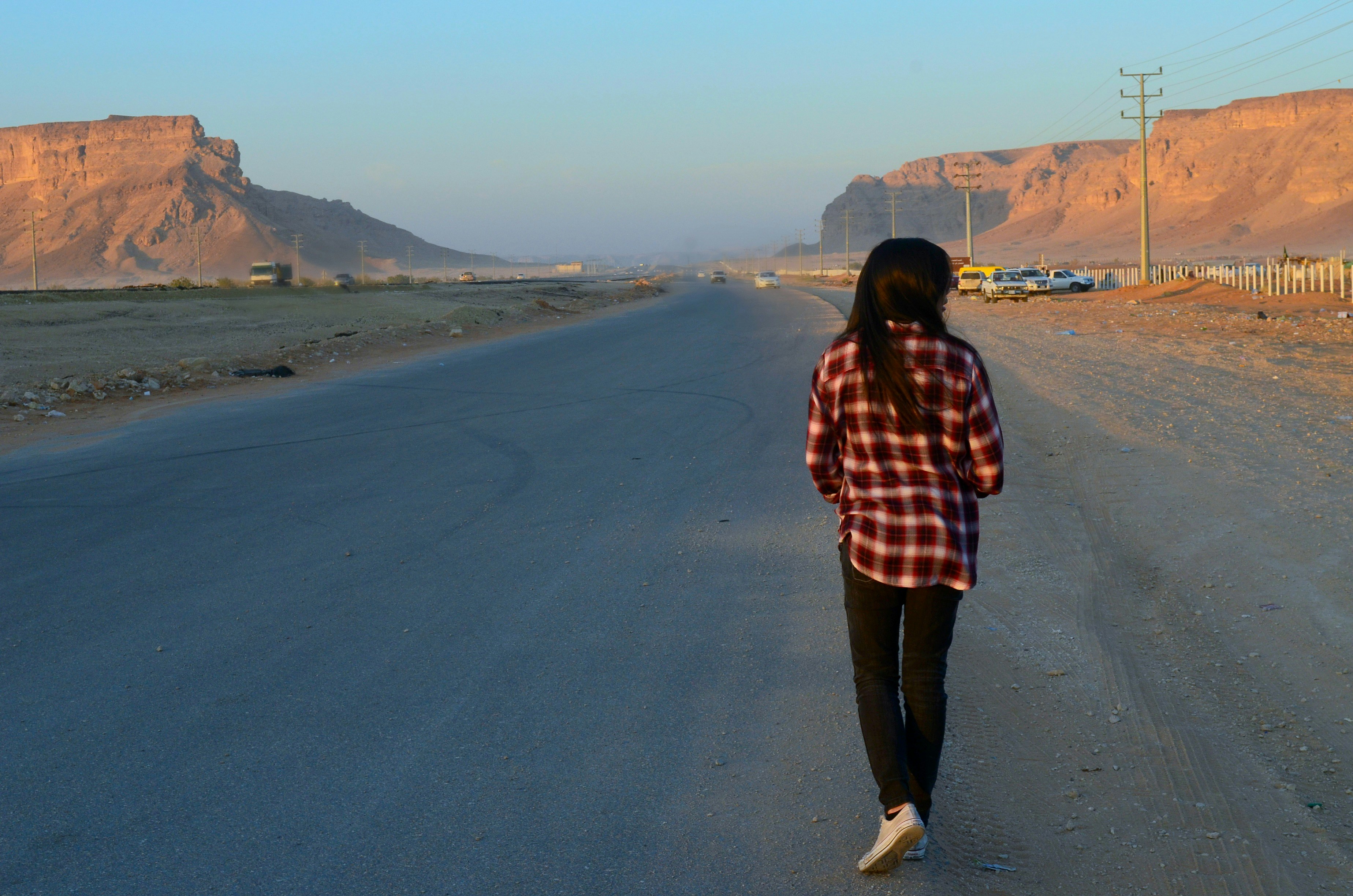 Person walking on empty road toward distant mountains, overcast sky, muted tones, cinematic wide shot