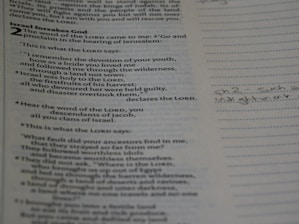 Close-up of hands holding a Bible with notes and a pen nearby.