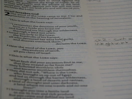 A close-up of hands holding an open Bible with highlighted verses and notes.